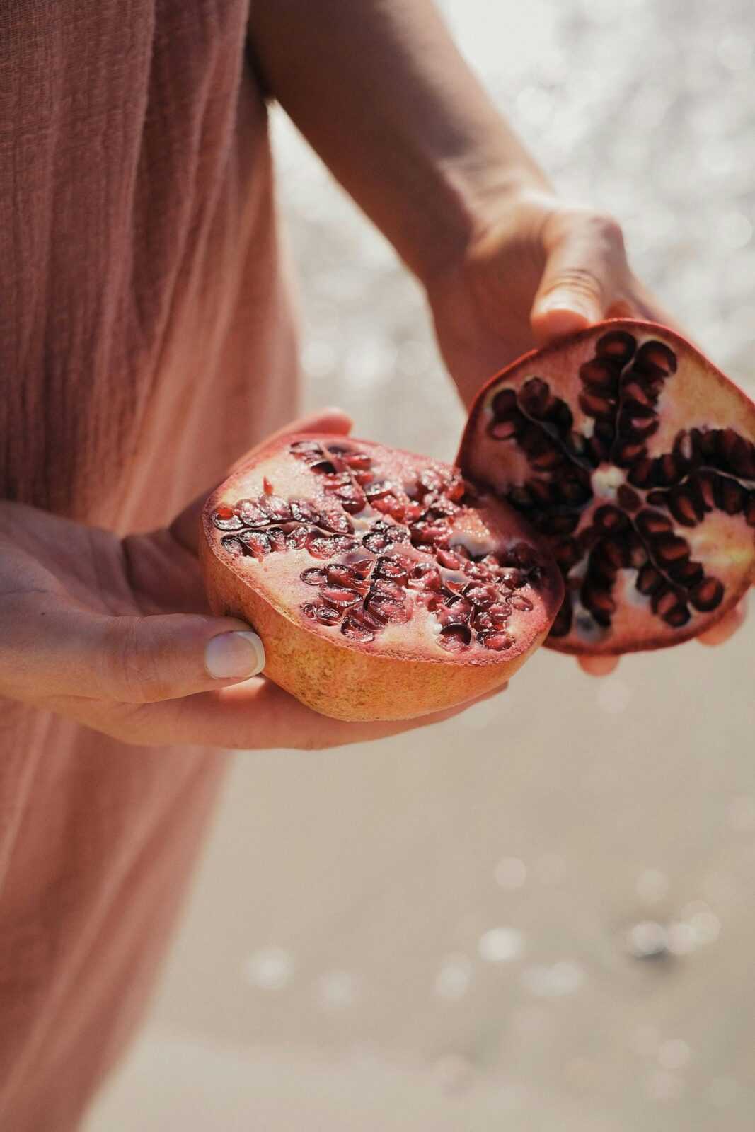 Close-up of hands holding a ripe pomegranate cut open by the seaside.