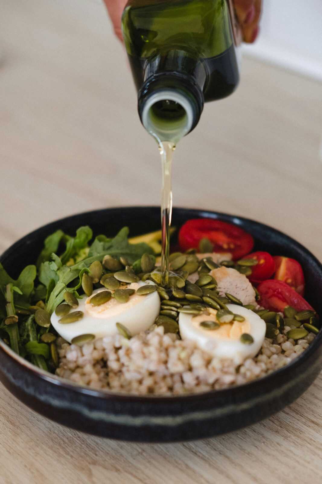 Delicious whole grain salad with fresh vegetables, pumpkin seeds, and olive oil pour.